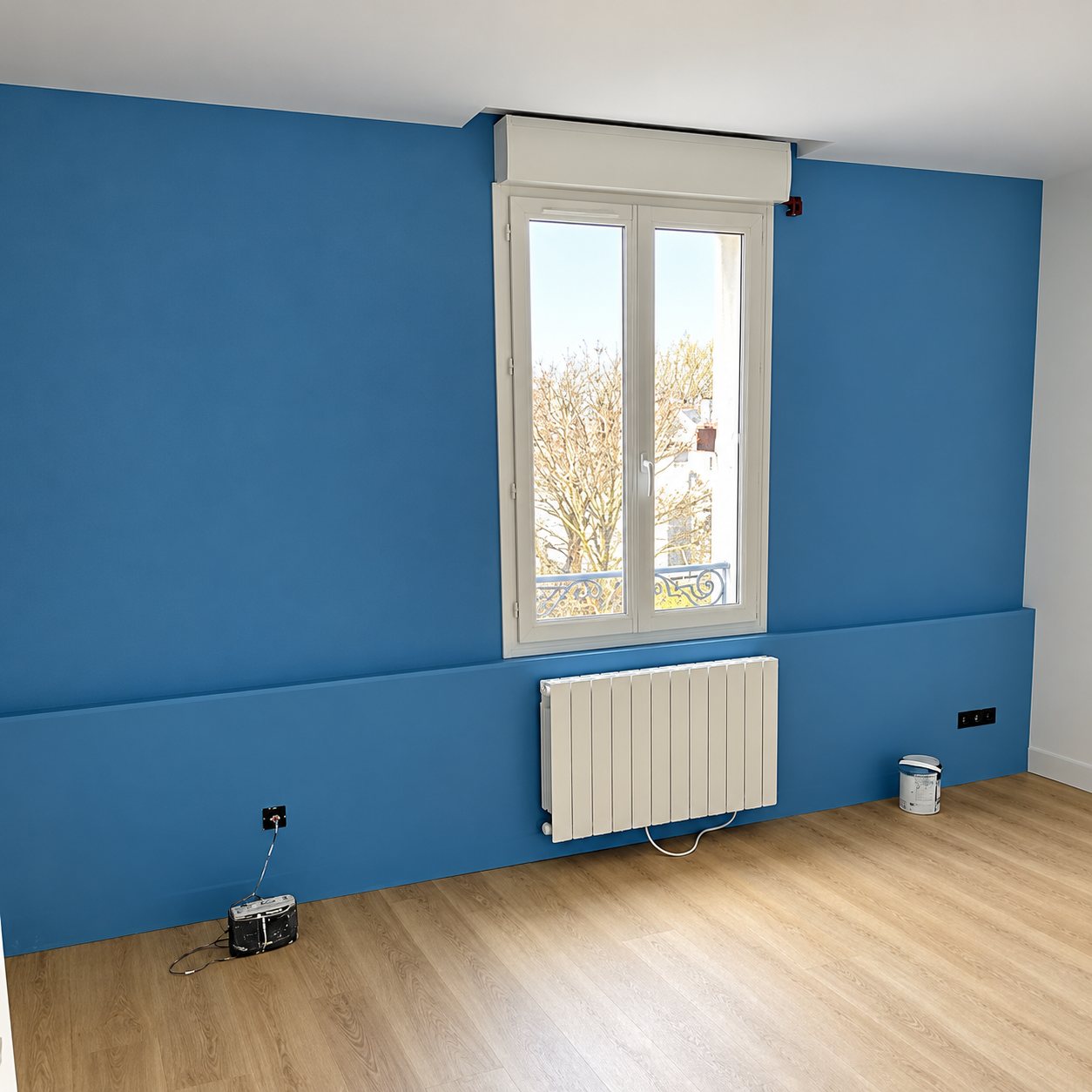 Pièce vide fraîchement peinte en bleu avec une fenêtre blanche, un radiateur et un parquet clair.
