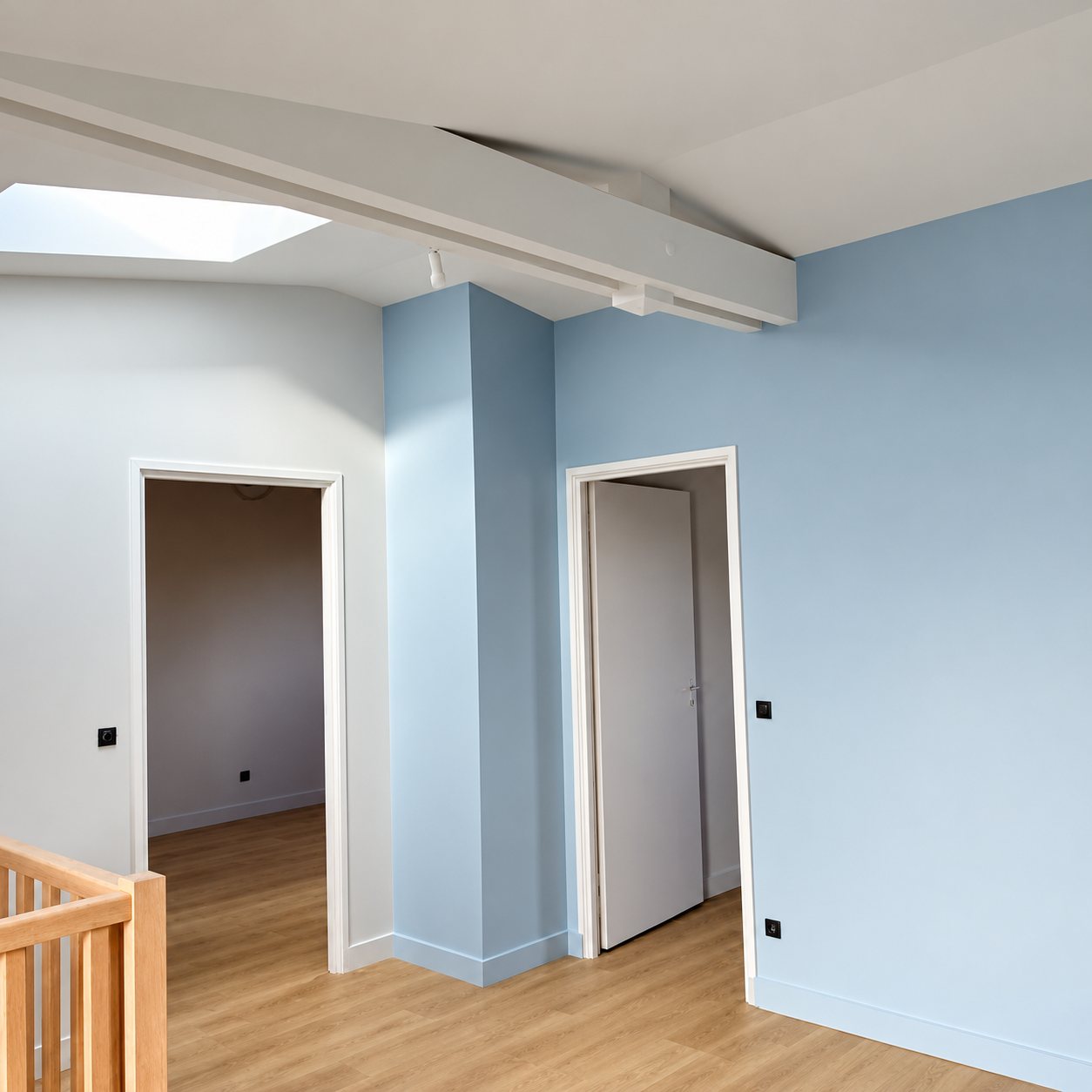 Palier d'étage récemment rénové avec murs peints en bleu clair, poutre blanche, fenêtre de toit, deux portes et parquet clair.
